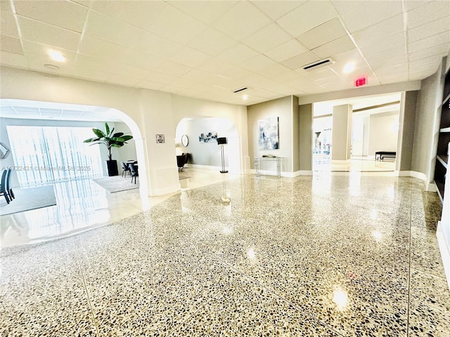 interior space featuring baseboards, visible vents, arched walkways, speckled floor, and a paneled ceiling