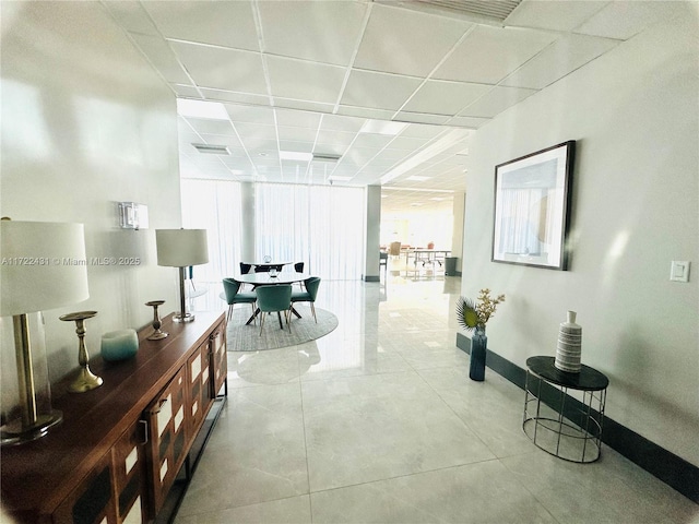 hall featuring a paneled ceiling, visible vents, baseboards, and tile patterned floors