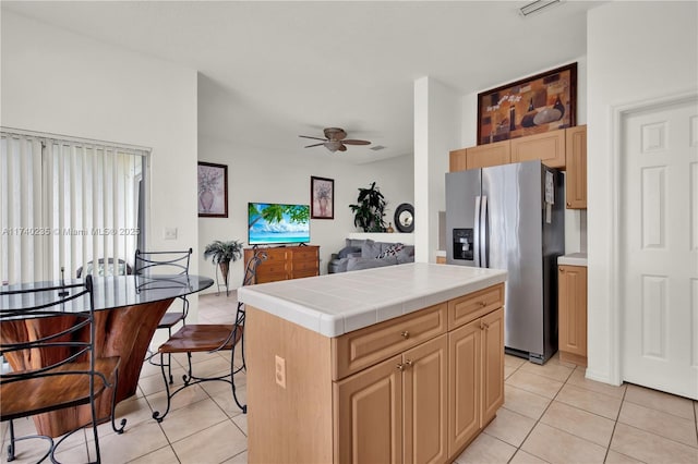 kitchen featuring tile counters, a center island, stainless steel fridge with ice dispenser, and light brown cabinetry