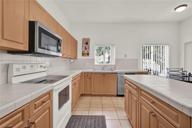 kitchen featuring sink, light tile patterned floors, stainless steel appliances, decorative backsplash, and tile countertops