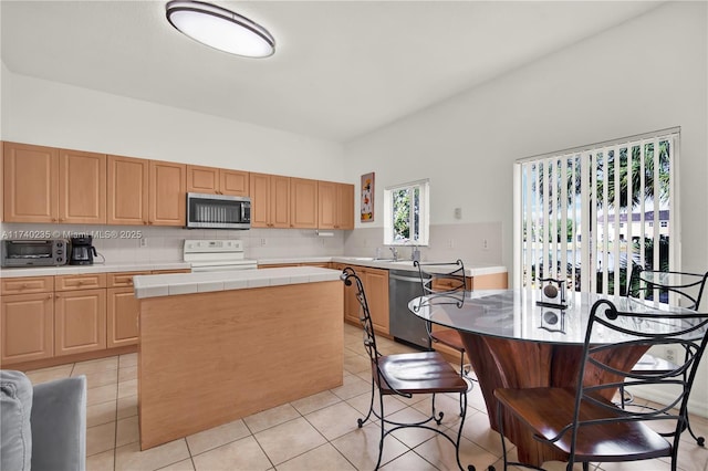 kitchen with backsplash, appliances with stainless steel finishes, a kitchen island, and light tile patterned floors