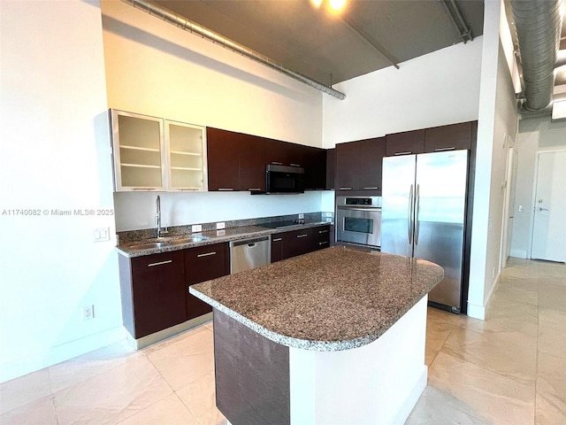 kitchen with a sink, a towering ceiling, appliances with stainless steel finishes, a center island, and dark stone counters