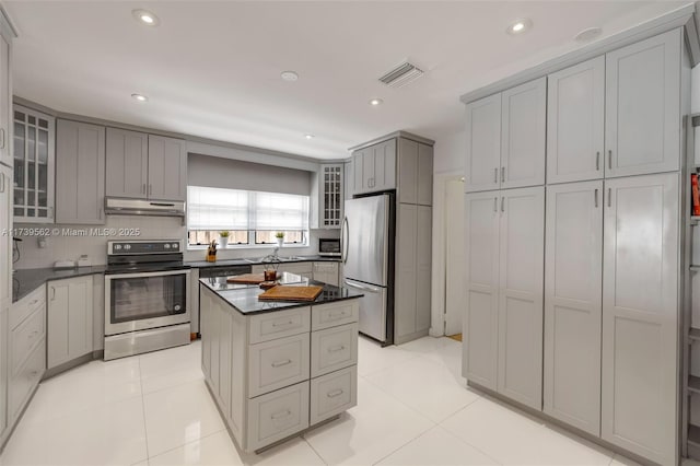 kitchen with gray cabinetry, a center island, dark stone counters, stainless steel appliances, and backsplash