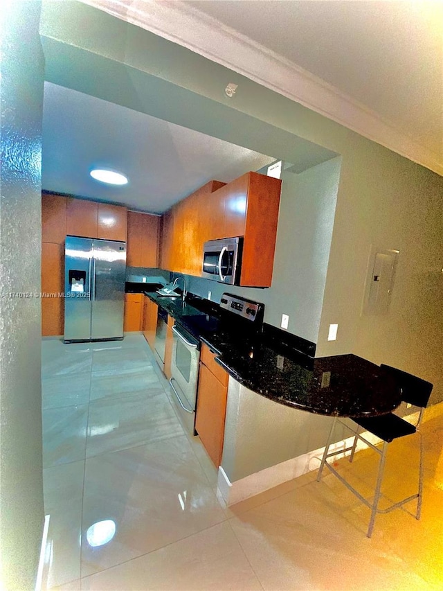 kitchen with light tile patterned floors, ornamental molding, dark stone counters, and appliances with stainless steel finishes