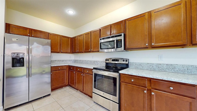 kitchen featuring light tile patterned flooring, appliances with stainless steel finishes, and light stone counters