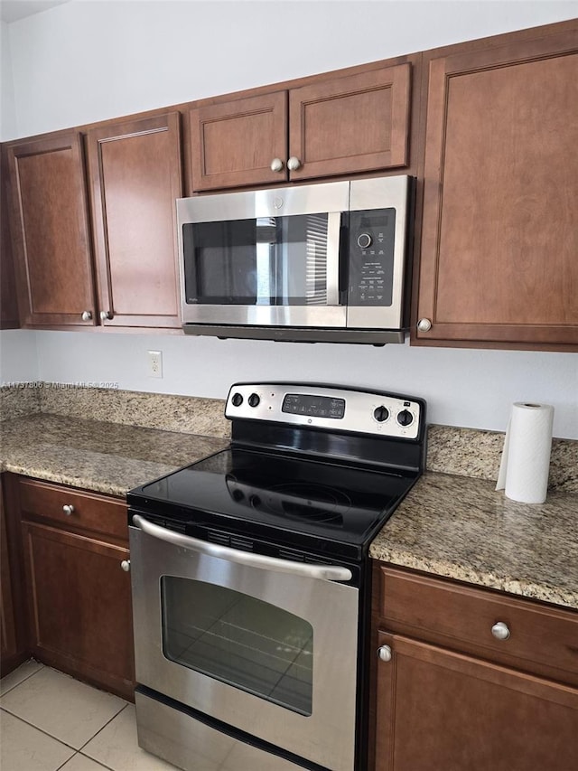 kitchen with light tile patterned flooring, stainless steel appliances, and stone countertops