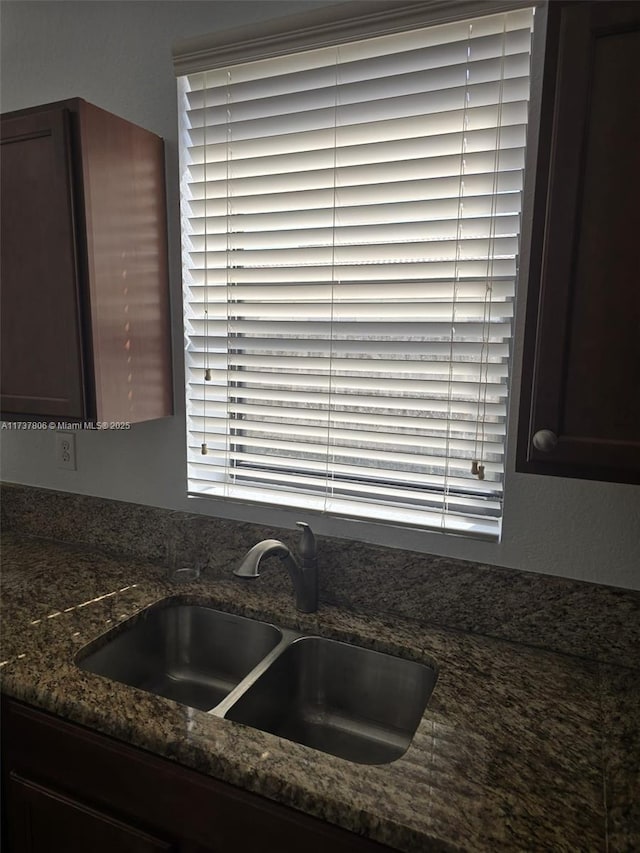 kitchen featuring sink, dark brown cabinetry, and dark stone counters