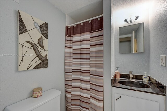 bathroom featuring vanity, a textured ceiling, toilet, and walk in shower