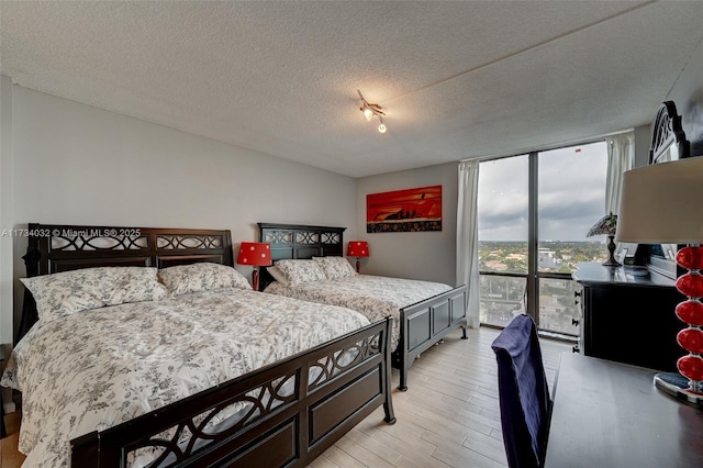 bedroom featuring floor to ceiling windows, light hardwood / wood-style flooring, and a textured ceiling