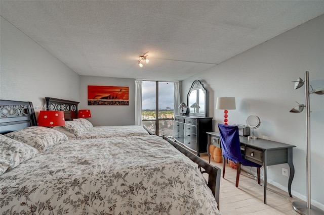 bedroom with a wall of windows, light hardwood / wood-style floors, and a textured ceiling