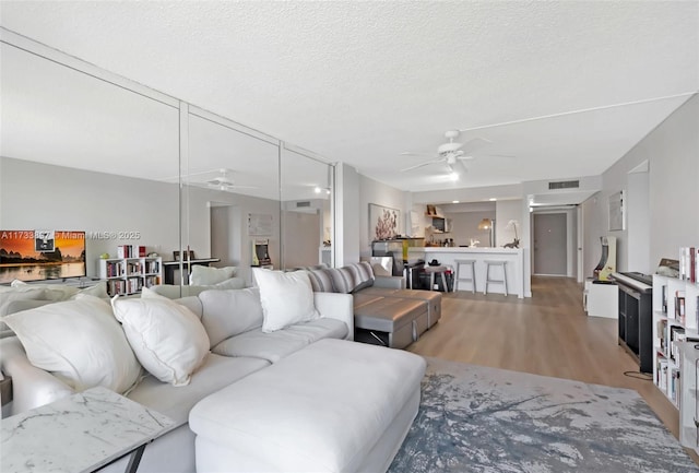 living area with ceiling fan, visible vents, light wood-style flooring, and a textured ceiling