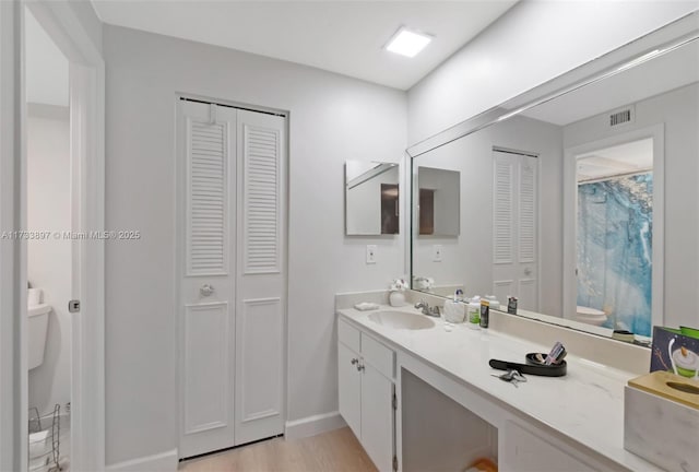 full bathroom with a closet, visible vents, toilet, vanity, and wood finished floors