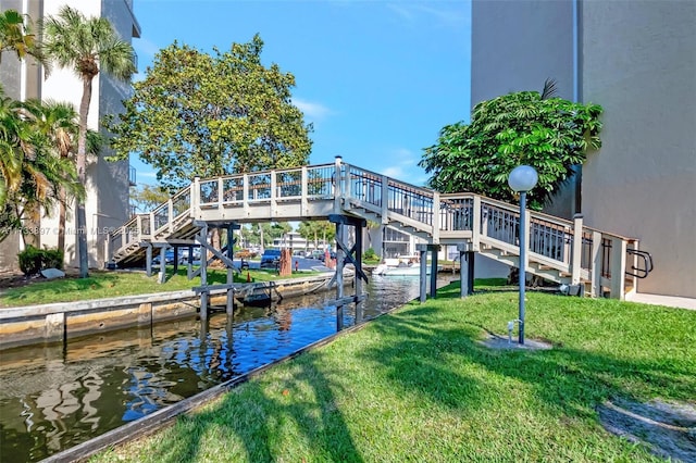 view of dock with stairway, a water view, and a lawn