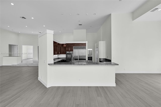 kitchen with dark brown cabinetry, kitchen peninsula, dark stone countertops, and built in refrigerator