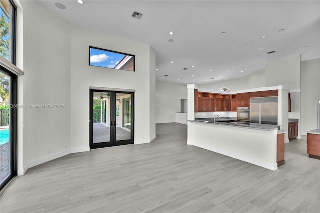 kitchen with built in refrigerator, a towering ceiling, light wood-type flooring, and french doors