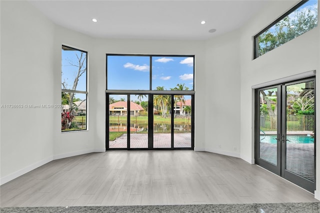 unfurnished room featuring a high ceiling, light wood-type flooring, and french doors