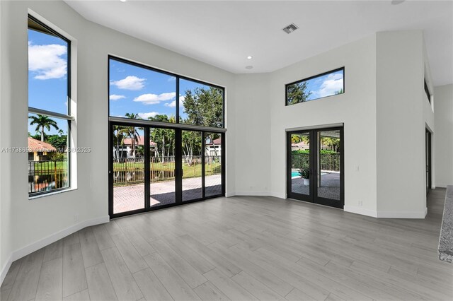 spare room featuring a towering ceiling, light hardwood / wood-style floors, and french doors