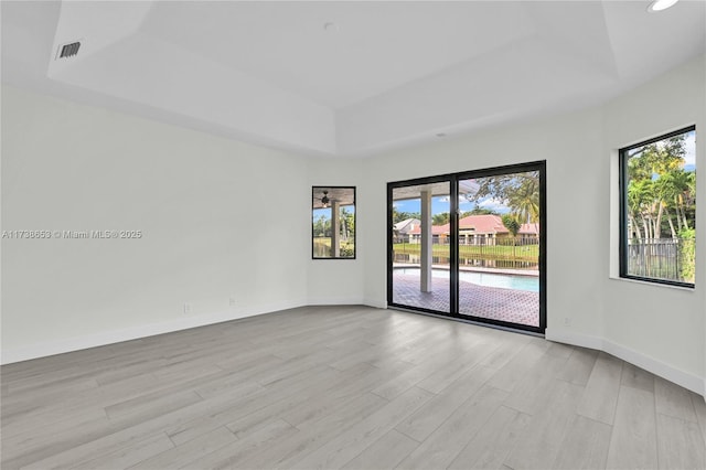 empty room featuring a tray ceiling and light hardwood / wood-style floors