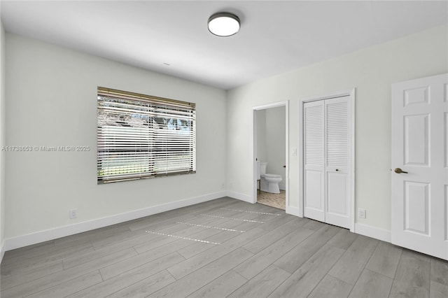 unfurnished bedroom featuring ensuite bath, light hardwood / wood-style flooring, and a closet