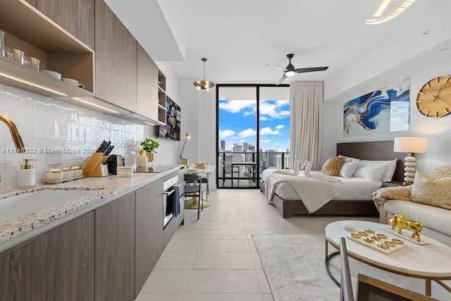 bedroom with light tile patterned flooring, floor to ceiling windows, sink, ceiling fan, and access to exterior