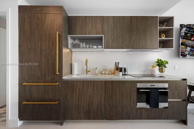 kitchen with tasteful backsplash, sink, oven, light stone counters, and dark brown cabinetry