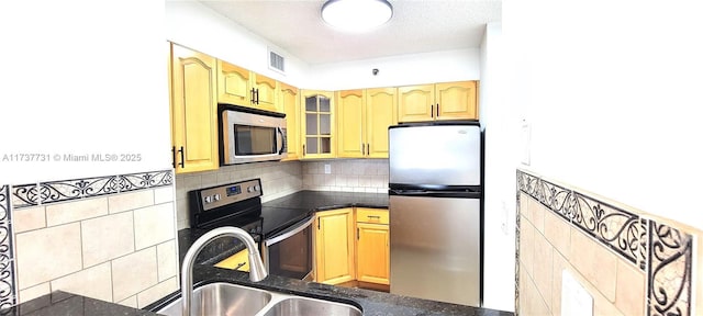 kitchen with sink, tile walls, backsplash, stainless steel appliances, and a textured ceiling