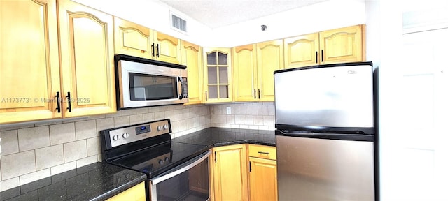 kitchen featuring appliances with stainless steel finishes, dark stone counters, a textured ceiling, and decorative backsplash