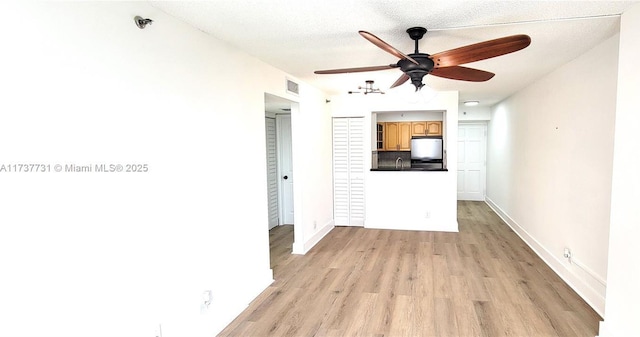 interior space featuring refrigerator, sink, ceiling fan, light hardwood / wood-style floors, and a textured ceiling