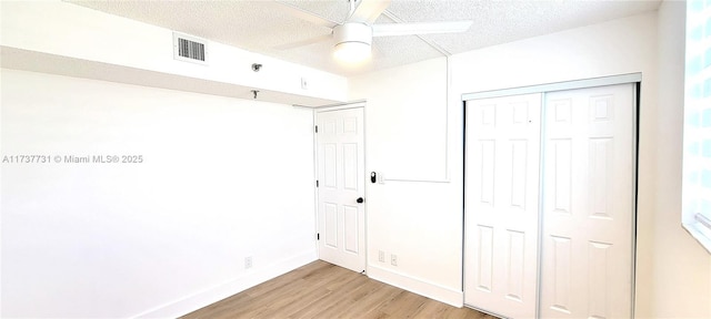 unfurnished bedroom featuring ceiling fan, a textured ceiling, light hardwood / wood-style floors, and a closet