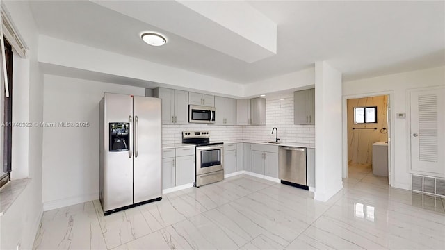 kitchen with tasteful backsplash, appliances with stainless steel finishes, gray cabinets, and sink