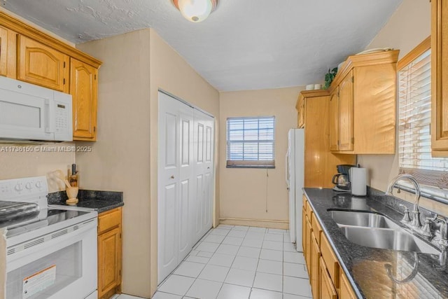 kitchen with sink, white appliances, light tile patterned floors, and dark stone counters