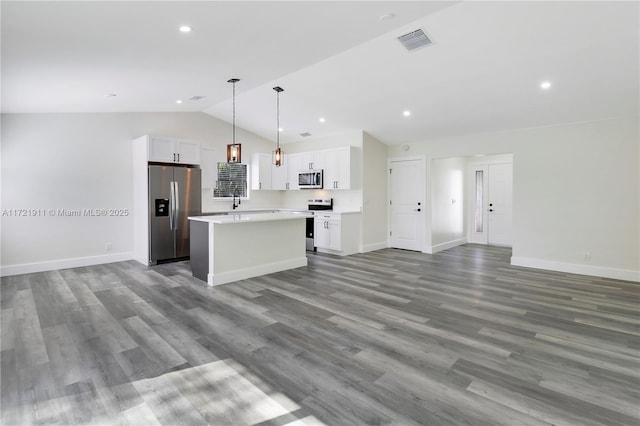 kitchen featuring stainless steel appliances, decorative light fixtures, a kitchen island, vaulted ceiling, and white cabinets