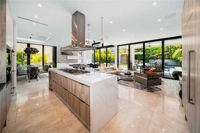 kitchen with a healthy amount of sunlight, island range hood, light stone counters, and a wall of windows