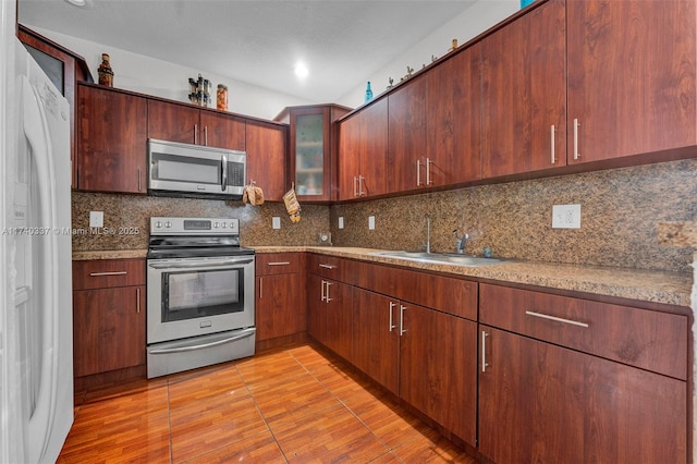 kitchen with sink, light stone counters, light wood-type flooring, stainless steel appliances, and decorative backsplash