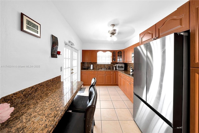 kitchen featuring sink, dark stone countertops, light tile patterned floors, stainless steel fridge, and backsplash