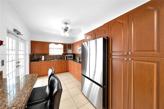 kitchen featuring light tile patterned flooring, sink, tasteful backsplash, dark stone countertops, and stainless steel refrigerator