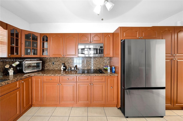 kitchen featuring tasteful backsplash, dark stone counters, light tile patterned floors, ceiling fan, and stainless steel appliances