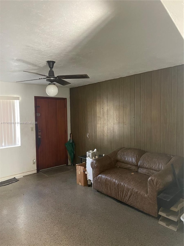 living room featuring ceiling fan, a textured ceiling, and wooden walls