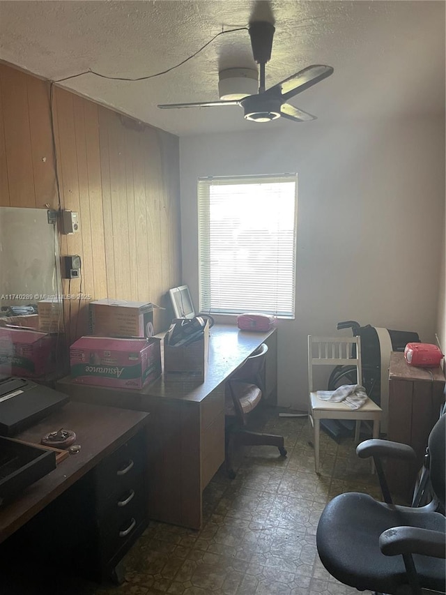 office area with a textured ceiling, wooden walls, and ceiling fan