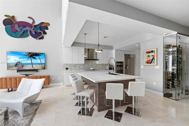 kitchen with appliances with stainless steel finishes, a center island with sink, a kitchen bar, decorative light fixtures, and wall chimney exhaust hood