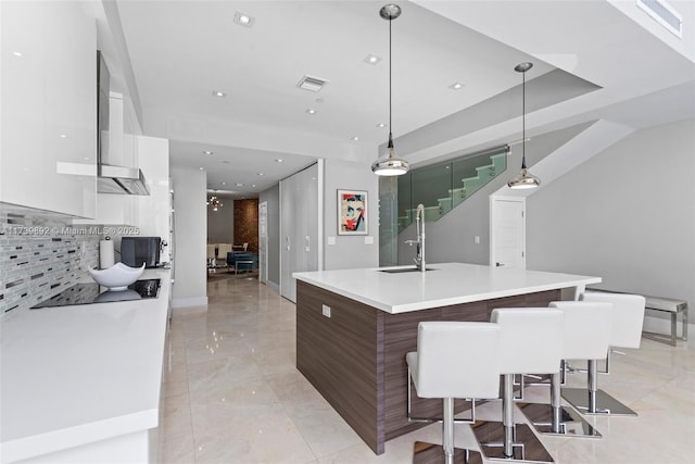 kitchen featuring a breakfast bar, pendant lighting, white cabinetry, an island with sink, and decorative backsplash