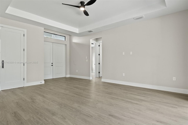 unfurnished bedroom with two closets, light hardwood / wood-style flooring, a raised ceiling, and ceiling fan