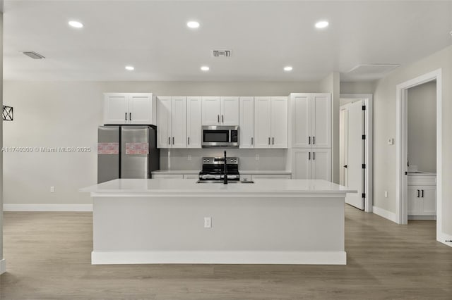 kitchen with stainless steel appliances, an island with sink, white cabinetry, and light hardwood / wood-style flooring