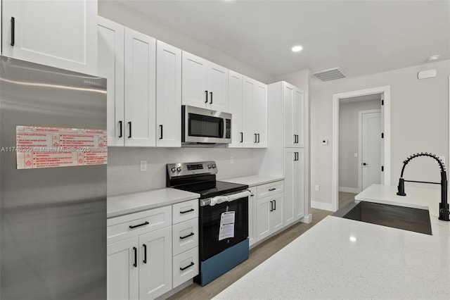 kitchen featuring appliances with stainless steel finishes, white cabinetry, sink, backsplash, and light stone countertops