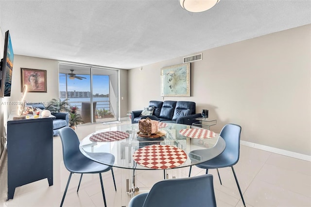 dining room featuring ceiling fan, expansive windows, a textured ceiling, and a water view