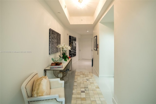 hallway featuring a tray ceiling and baseboards