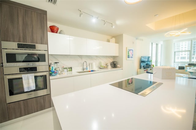 kitchen with a sink, stainless steel double oven, light countertops, decorative backsplash, and black electric stovetop