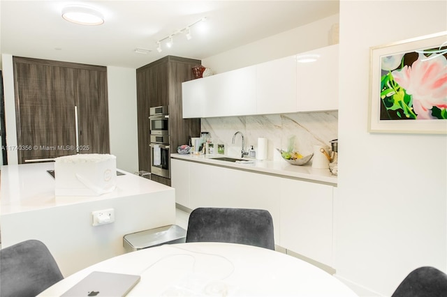 kitchen with backsplash, white cabinets, light countertops, and a sink