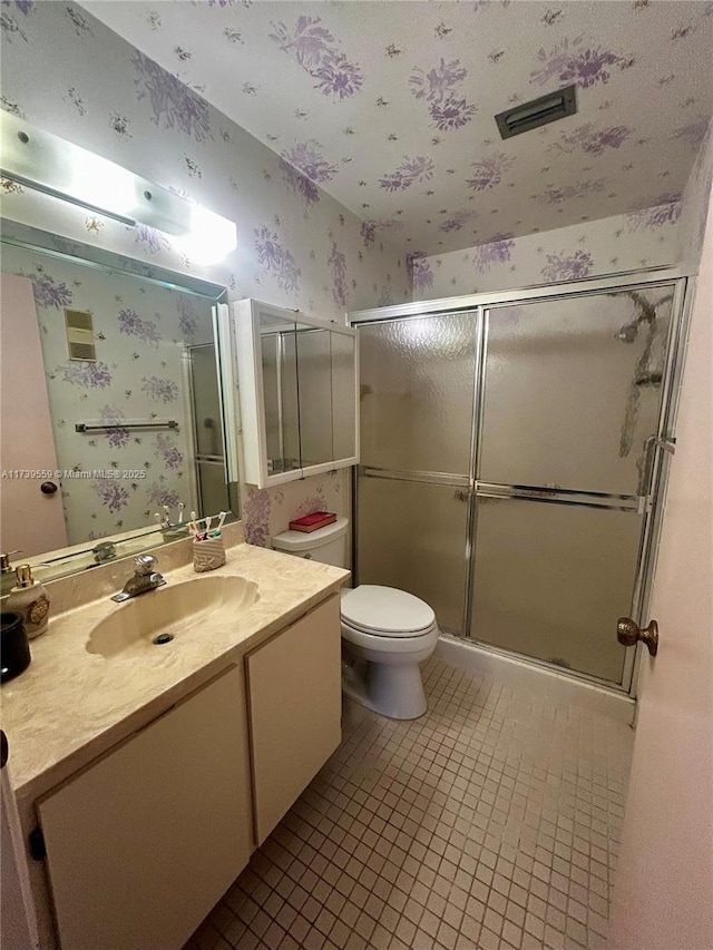 bathroom featuring a shower with door, vanity, tile patterned floors, and toilet