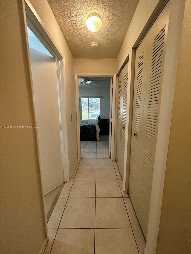 corridor featuring light tile patterned flooring and a textured ceiling